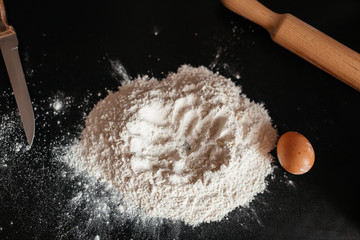 girl kneads dough on a black table with eggs and flour