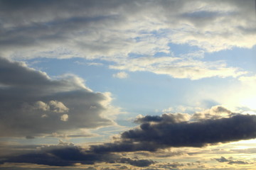 Clouds in the blue sky at sunset or dawn backlit by the sun. Place for text and design.