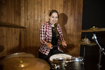 Professional drum set closeup. Beautiful young girl drummer in checkered shirt with drumsticks playing drums and cymbals, on the live country or rock music concert or in recording studio. Female drumm