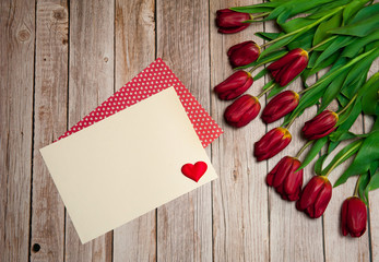 Flower composition. Paper blank and a spring bouquet of red tulips on a wooden background. Free space.
