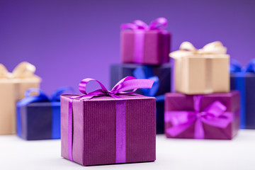 Present. Gift boxes in multicolored paper with lilac ribbons, on a purple background. Happy Holidays.