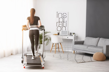 Sporty young woman training on treadmill at home - obrazy, fototapety, plakaty