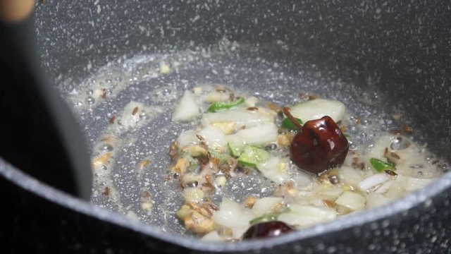 Frying Onions with green chilies, garlic, ginger and cumin seeds to make Tadka to make of spicy Indian lentils called Daal tadka. A 4K video resolution.