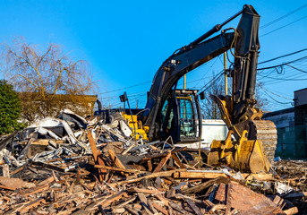 Fototapeta premium Demolition bulldozer in midst of building rubble. Bucket is down, side view. Yellow construction machine with buildings in background.
