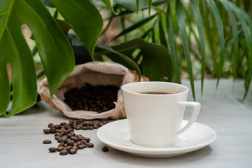 Obraz na płótnie Canvas Cup coffee with sack roasted coffee bean against palm leaves background.