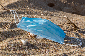 Medical protective mask is left abandoned on the beach. It must be disposed in a proper hazardous waste bin, preventing germs spread. Objects and medical supply waste management.