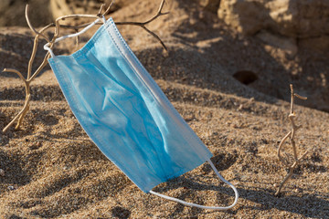 Medical protective mask is left abandoned on the beach. It must be disposed in a proper hazardous waste bin, preventing germs spread. Objects and medical supply waste management.