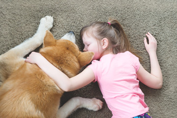 young girl hugging her dog on the carpet, friendship concept