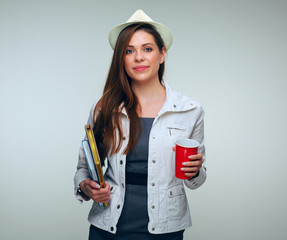 Woman student dressed white jacket and holding big red coffe cup and books.
