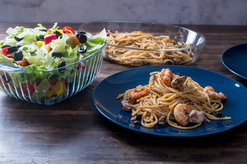 Delicious fresh home made seafood spaghetti  with squid and prawn served on top of wooden table background with salad and sprinkled cheese