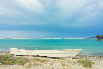 Fototapeta premium Wooden white boat parking on the sea sand beach over blue water and sky background, Bahrain.