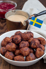 Meatballs served with cream sauce and cranberry jam,  in white bowl with swedish flag, vertical