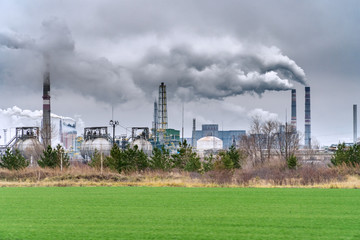 View of a chemical plant with Smoking chimneys against a dark cloudy dirty sky