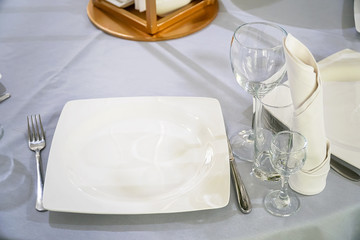 The table in the restaurant is served for dinner. On a table with a white tablecloth, empty wine glasses, a plates, napkins. Selective focus