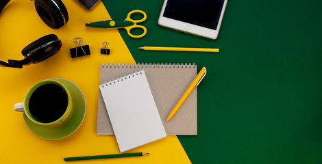 Notebook and pen with a place for writing. Workspace with stationery, top view. Remote remote work online. Study and creativity. Yellow and green background with a cup of coffee and headphones.
