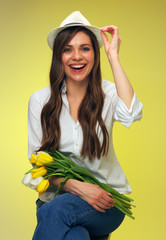 Portrait of smiling woman holding flowers touching her hat