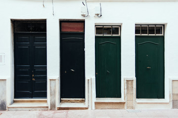 Unique image of four dark green doors on a white wall.