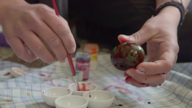 Footage of greek caucasian family, preparing coloured eggs for Easter, during coronavirus lockdown. Close up of woman's hands painting an egg with brush