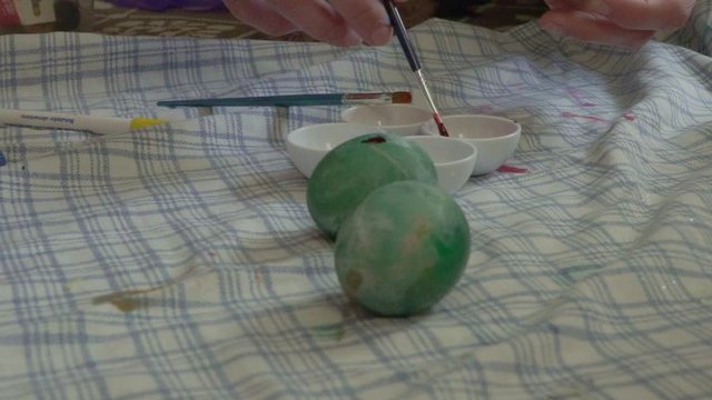Close up slow motion, push in shot of caucasian woman, painting eggs for easter with a brush