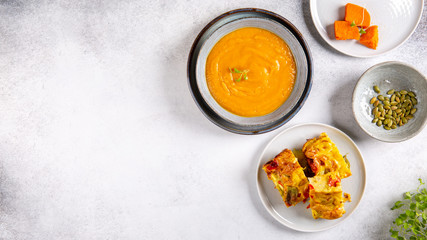 Vegetarian lunch -  sweet potato cream soup and savory vegetable pie on concrete background. Top view, copy space.
