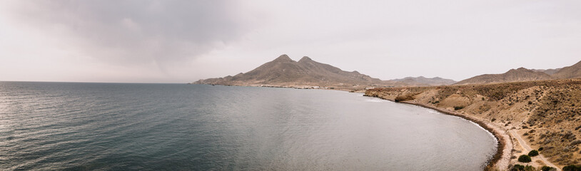 Maritime panoramic view of a sea inlet next to the desert coast with cloudy sky.