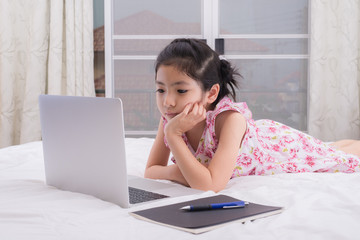 A girl is using a computer in her bed to study online at home while detained at home during the Covid-19 virus outbreak.