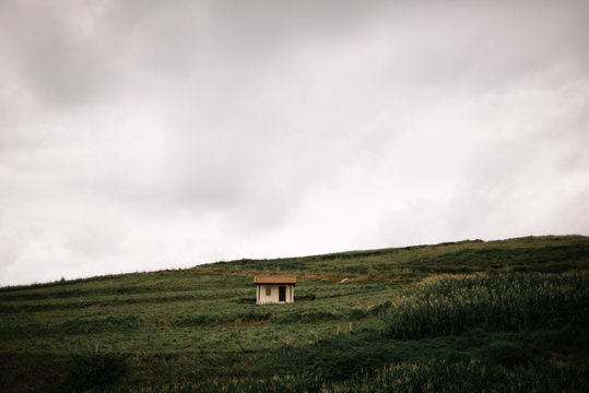 Unique grazing cabin in the middle of a green hill and a big gray and cloudy sky.