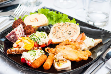 plate with a variety of foods, meat, vegetables, cheese, salami and fried foods on a wooden table