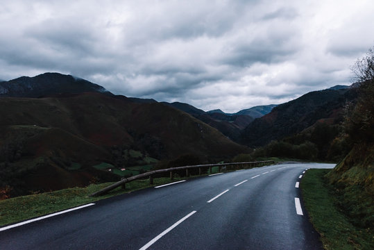Picturesque image of rural road between dark green mountains on a wet and cloudy gray day