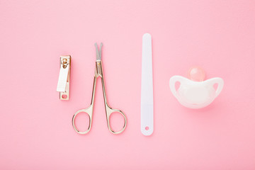 Scissors, clipper, nails file and soother on light pink table. Pastel color background. Baby nails grooming. Closeup. Top down view.
