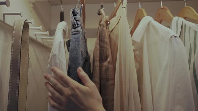 Close-up of female hands open clothing closet and stroke her hand on hangers with clothes . Clothes on hanger in home wardrobe with LED light. 4k footage. Dolly shot from the side