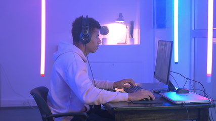 Profile view of handsome multiracial gamer taking headphones on and starting playing online video game.