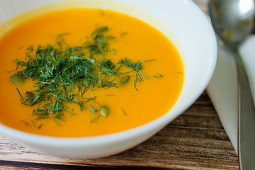 Traditional pumpkin soup with seeds, dill on a wooden table close up.