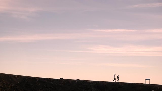 Silhouette of day hikers walking along a distant barren ridgeline trail during golden hour on Haleakala, Red Hill