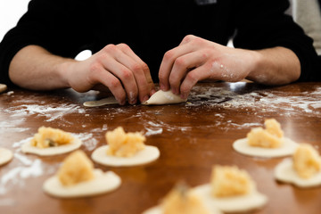Obraz na płótnie Canvas modeling dumplings over a wooden table,in the hands of the dough,cooking for european recipe,flour on the background of hands with dumpling