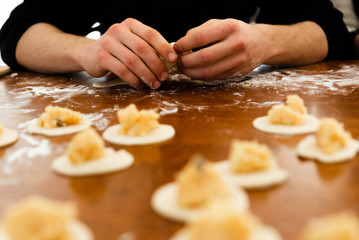 modeling dumplings over a wooden table,in the hands of the dough,cooking for european recipe,flour on the background of hands with dumpling