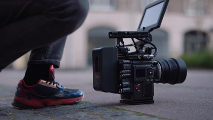 Female filmmaker and cinematographer puts v lock battery on cinema camera on the ground