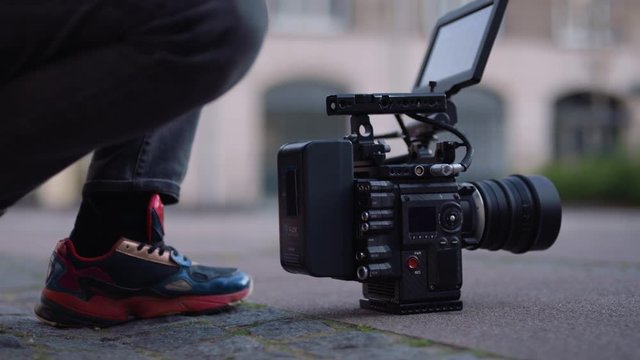 Female filmmaker and cinematographer puts v lock battery on cinema camera on the ground