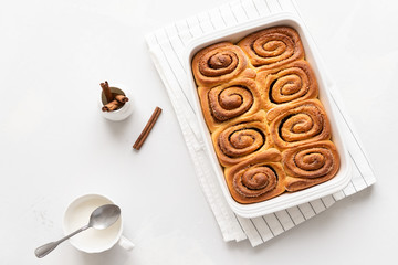 Freshly baked Cinnamon rolls or cinnabons in white ceramic dish and cream sauce in a cup on white background. Homemade buns. Bakery menu, recipe, pastry, cook book. Hygge. Top view