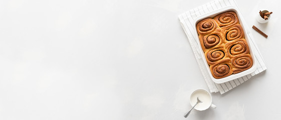 Bakery banner. Cinnamon rolls or cinnabon in ceramic baking dish on white background. Cinnabons recipe. Traditional homemade sweet buns. Pastry, bakery. Top view, copy space