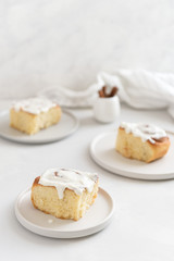 Fragrant freshly baked Cinnamon rolls or cinnabons covered with white cream glaze on the plates on white background. Cinnabons recipe. Traditional homemade sweet buns. Pastry, bakery. Copy space