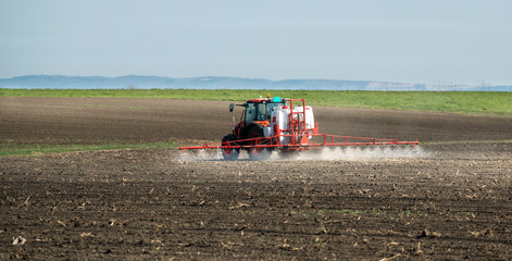 Fototapeta premium Tractor spraying land in sunset.