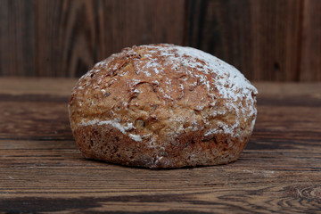 A view of fresh, dark, wholemeal bread sprinkled with flour. A freshly baked, hexagonal loaf on a wooden, rustic table with brown boards.