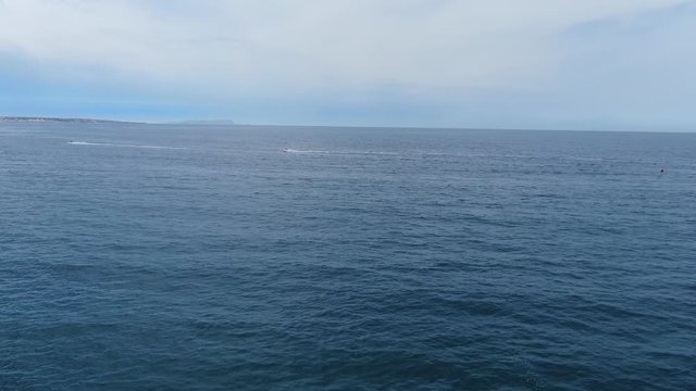 High aerial view of water skiers in distance in blue ocean water, one drives in foreground