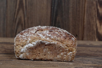 Side view of fresh bread sprinkled with flour. A freshly baked loaf on a wooden, brown, rustic table. In the background brown boards.