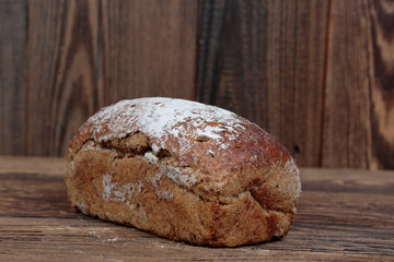 Fresh, molded bread sprinkled with flour. A freshly baked loaf on a wooden, brown, rustic table.