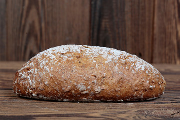 Side view of golden, fresh bread sprinkled with flour. A freshly baked loaf on a wooden, brown, rustic table. In the background brown boards.