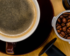 Coffee cup on wooden kitchen table with coffee beans. Top view with morning sunlight