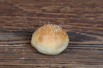 View, close-up of a handmade, fresh, round bread roll sprinkled with sesame seeds on a wooden, brown, rustic table.