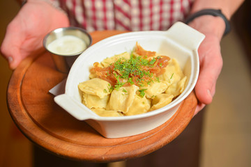 Waiter holds a plate of tasty Italian food Ravioli. Italian cuisine in restaurant, Ravioli dumplings with meat and sauce